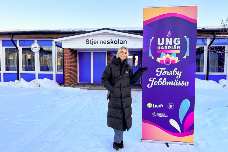 Kvinna i snö utanför Stjerneskolans entré, skylt med reklam för jobbmässa